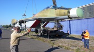 Jeřáb snáší MiG na zem před kbelským hangárem.