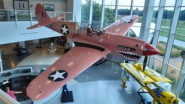 Růžový Curtiss P-40 Warhawk zavěšený v recepci muzea. V kokpitu je umístěna kombinéza paní Sue Parish.